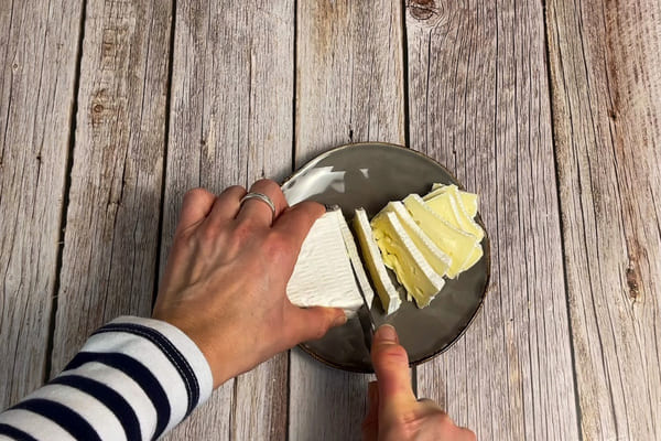 Camembert wird auf einem Teller in Scheiben geschnitten