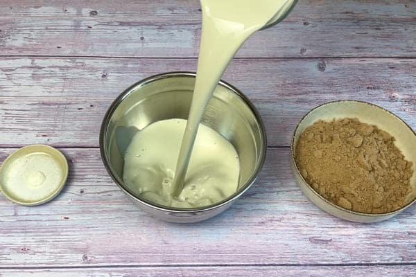 Für veganen High Protein Pudding wird Pflanzendrink in eine Rührschüssel gegossen und drum herum stehen Guarkernmehl und Schokoladen Proteinpulver.