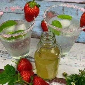 Eine Flasche mit Holunderblütensirup ohne Zucker und zwei Gläsern Hugo ohne Alkohol mit Erdbeeren
