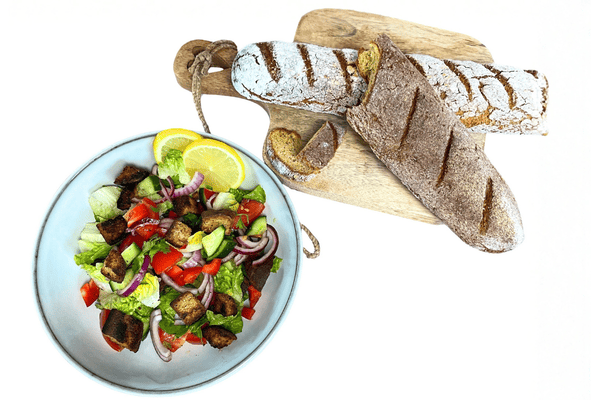 Mediterraner Brotsalat in einer Bowl und zwei low carb Baguettes auf einem Holzbrett