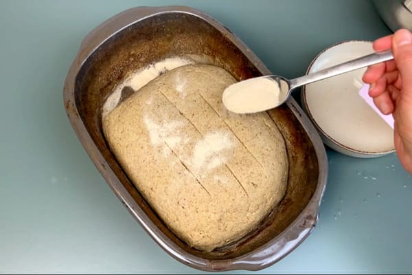 Ungebackenes low carb Joghurtbrot in einer Keramikbackform, das mit Kartoffelfasern bestreut wird