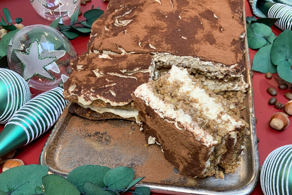 Angeschnittenes low carb Lebkuchen Tiramisu auf einem Tablett mit Kaffeebohnen, Haselnüssen und Weihnachtskugeln