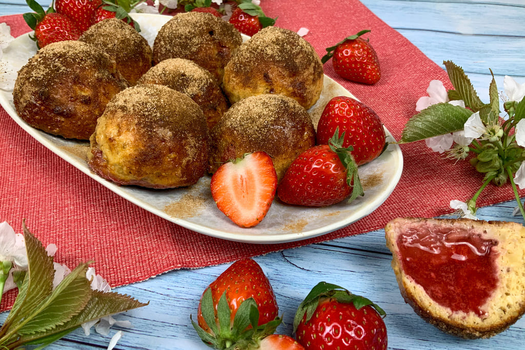 Low carb Quarkbällchen aus dem Backofen mit Erdbeeren und Zimt und Xucker bestreut auf einem Teller.