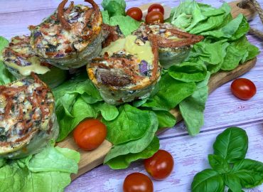 Vegetarische low carb Rührei Muffins mit Käse, Champignons und veganem Speck auf einem Salatbett mit Tomaten angerichtet.