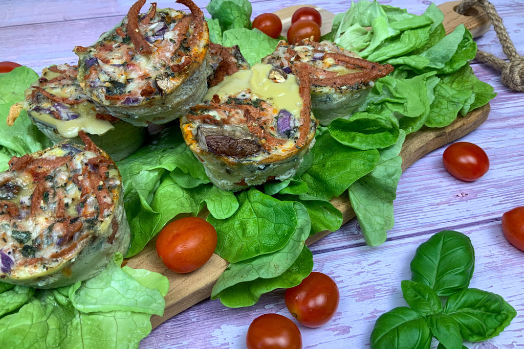Vegetarische low carb Rührei Muffins mit Käse, Champignons und veganem Speck auf einem Salatbett mit Tomaten angerichtet.