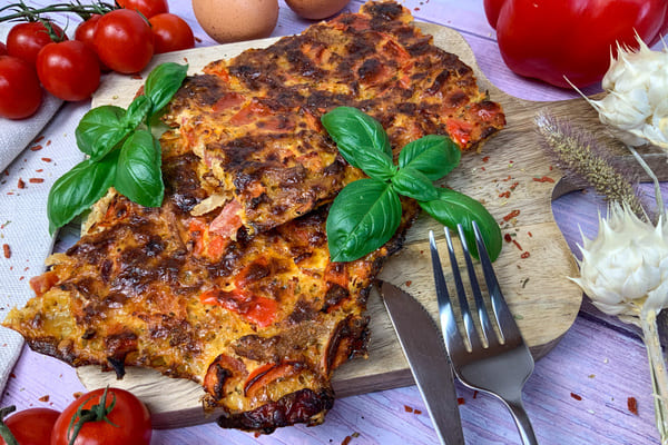 Fertig gebackene low carb Schüttelpizza auf einem Holzbrett mit Basilikum, Tomaten, Paprika und Eiern