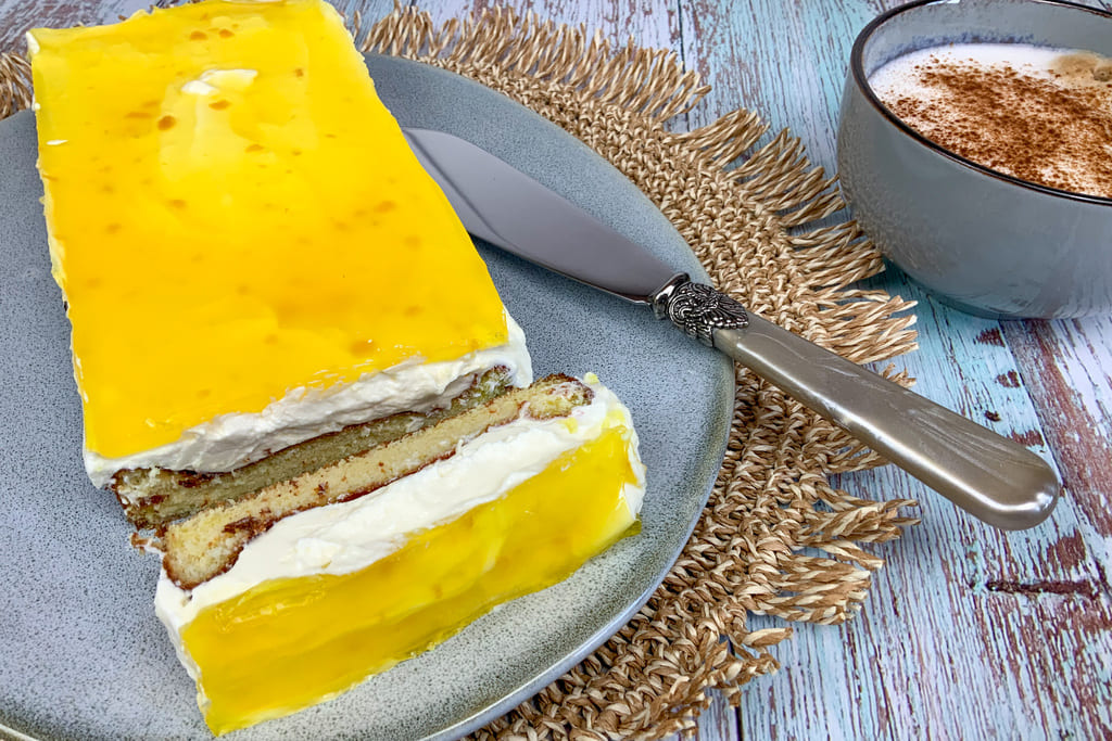 Mango Maracuja Quark Kuchen auf Teller mit Cappuccino serviert
