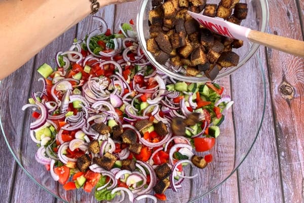 Mediterraner Brotsalat mit Tomaten, roten Zwiebeln, Gurken und Paprika wird mit gewürfeltem geröstetem low carb Brot getoppt