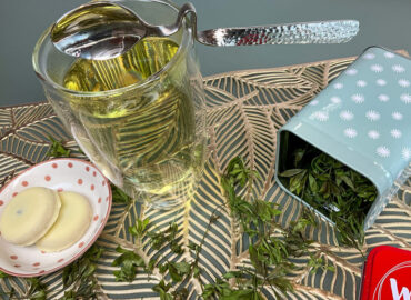 Waldmeister Tee selber machen: Eine Tasse Waldmeister Tee, ein kleiner Teller mit Keksen und eine Teedose mit getrocknetem Waldmeister